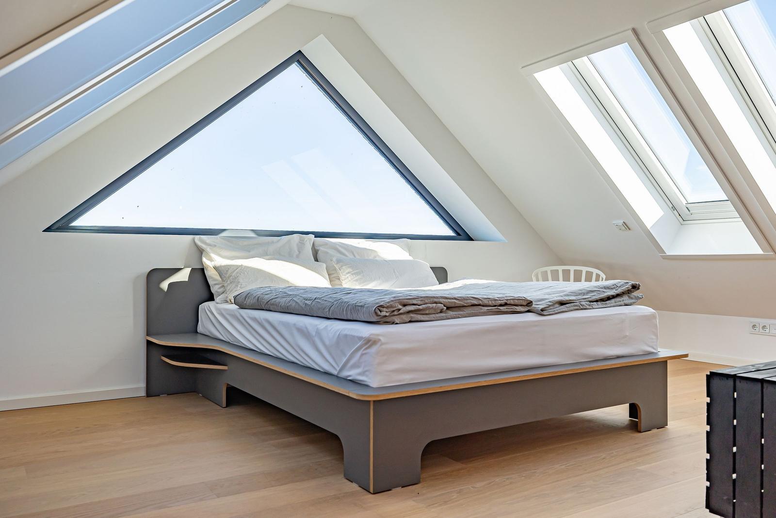 Schlafzimmer mit Dachschrägen, großem Fenster und Bett mit weißen Kissen.