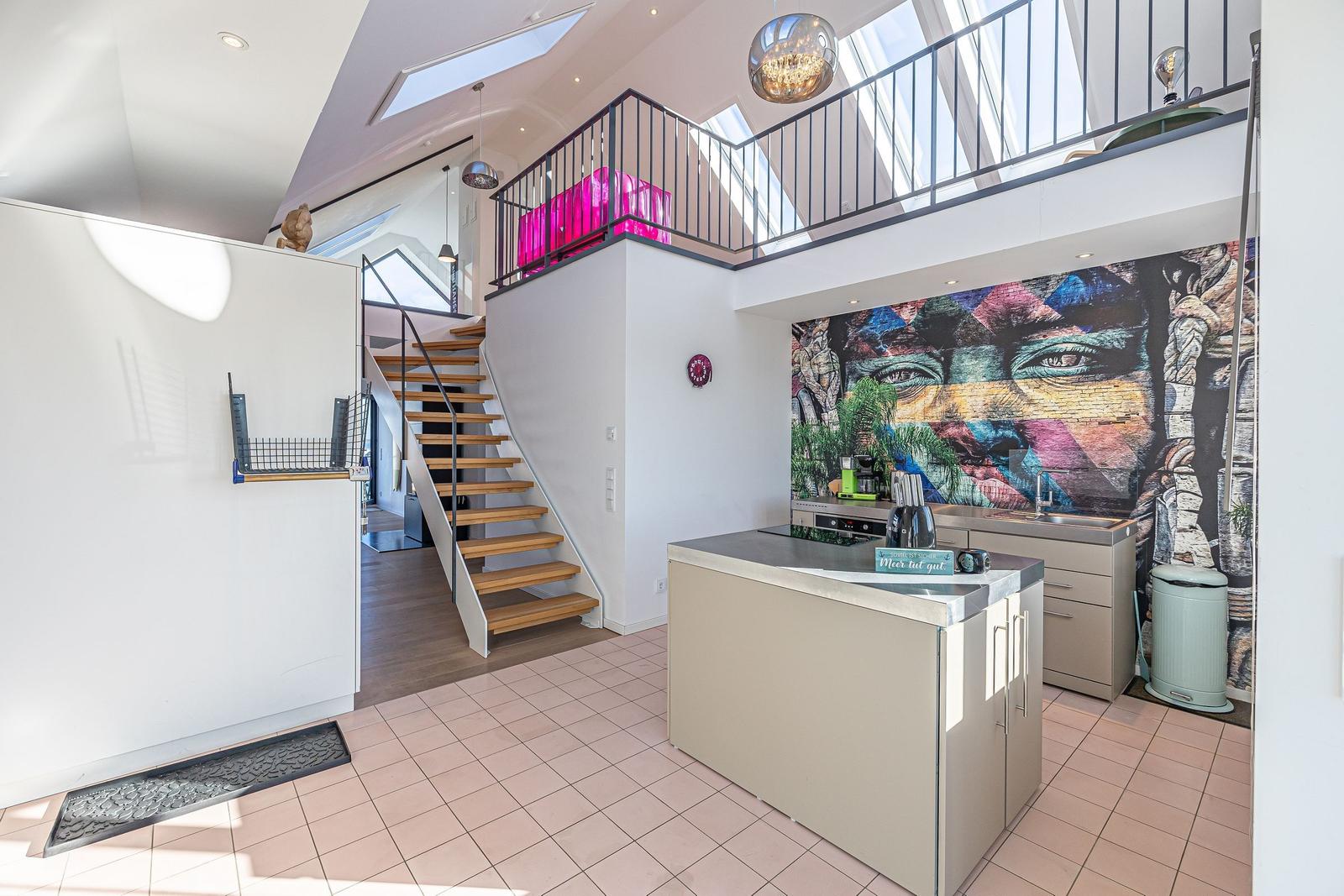 Küche mit Mural an der Wand, Treppe zur Galerie, helles Ambiente.