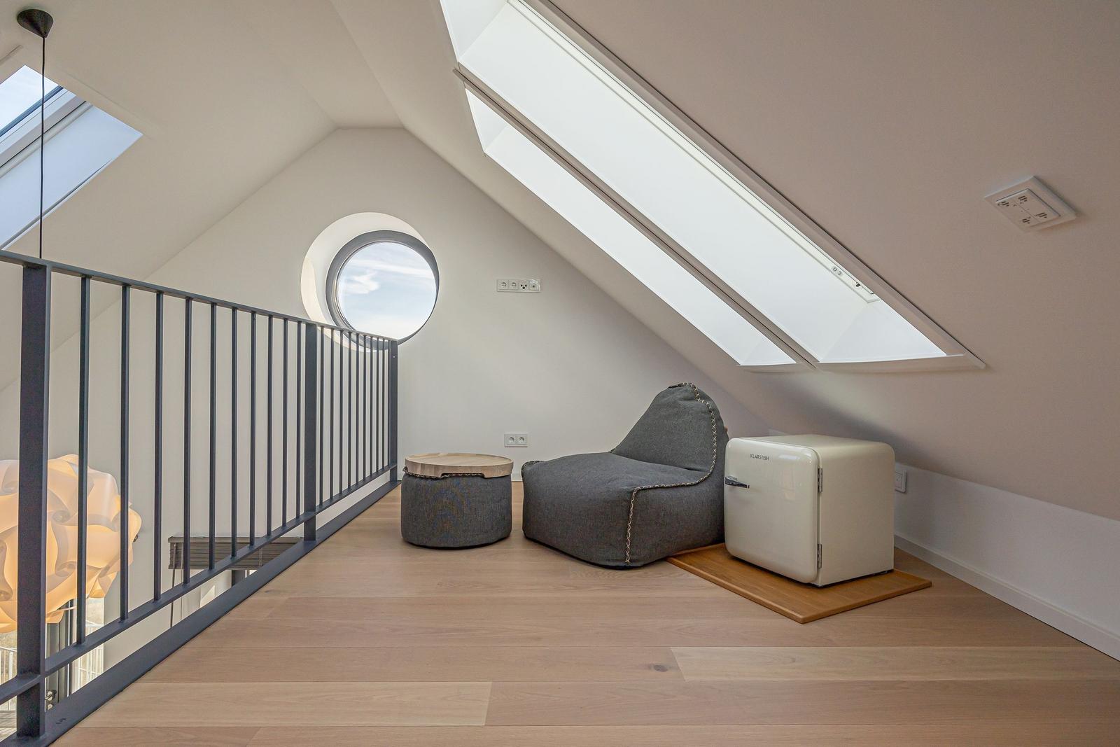Dachgeschosszimmer mit Sitzgelegenheit, runden Fenster und Dachfenstern.