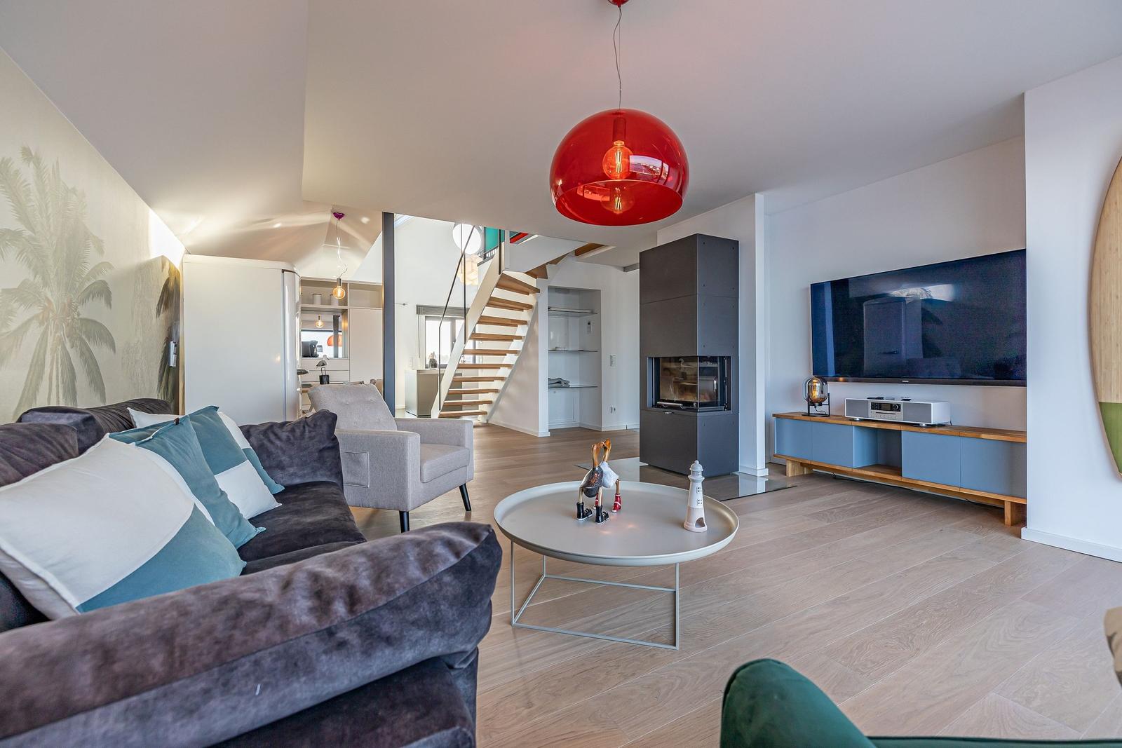 Wohnzimmer mit Sofa, Fernseher und Kamin. Rote Deckenlampe und Holzboden.