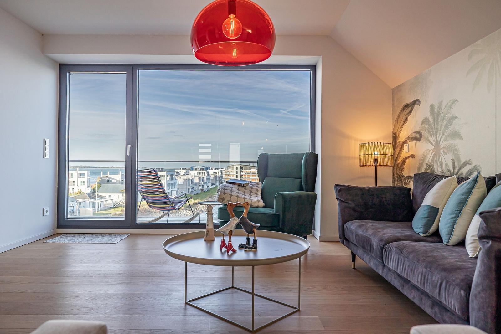 Wohnzimmer mit Blick aufs Meer, Sofa, Sessel und runder Tisch.
