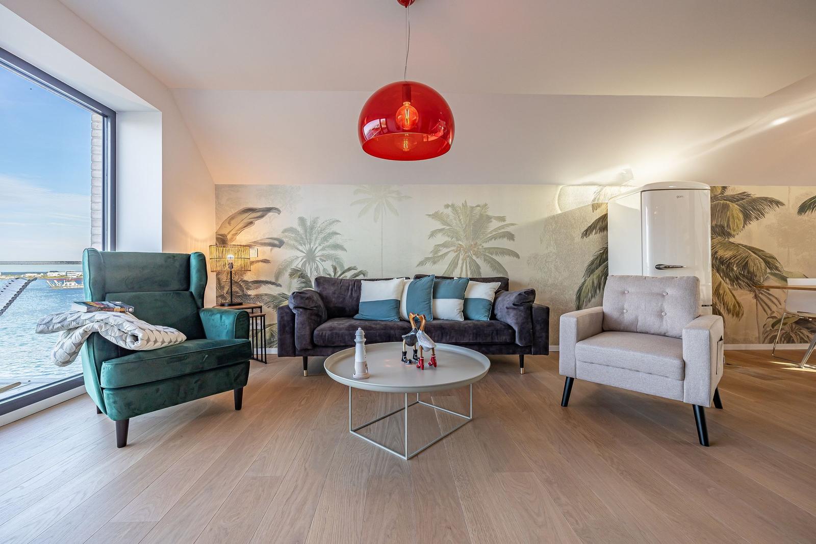 Wohnzimmer mit Sofa, Sesseln und Blick aufs Wasser.