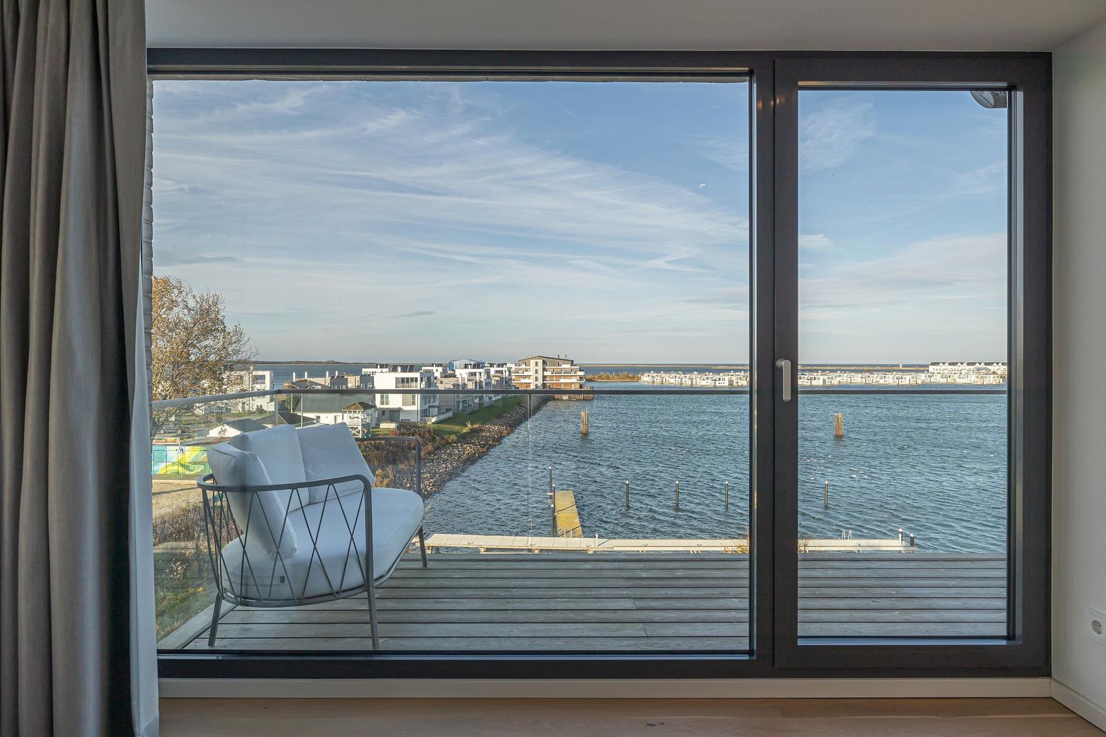 Blick auf Wasser und Ufer mit Liegeplatz vor großem Fenster.