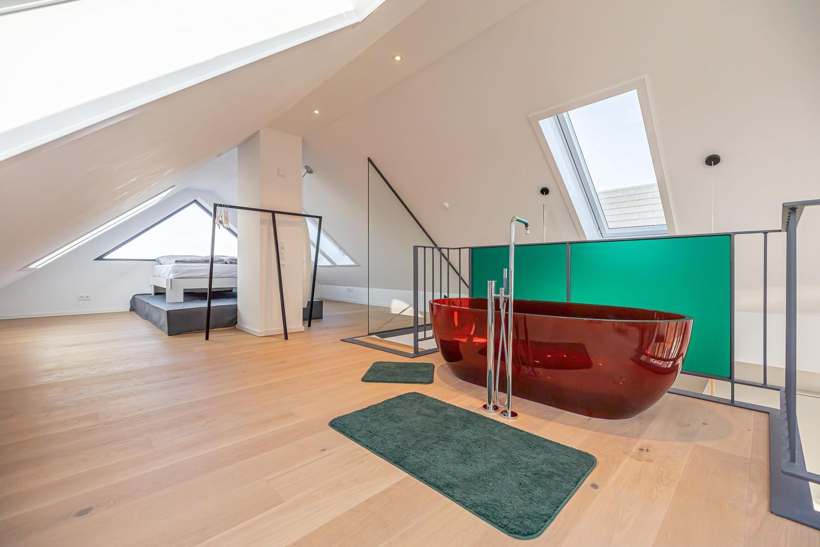 Dachgeschosszimmer mit roter Badewanne und Bett unter Dachschrägen.