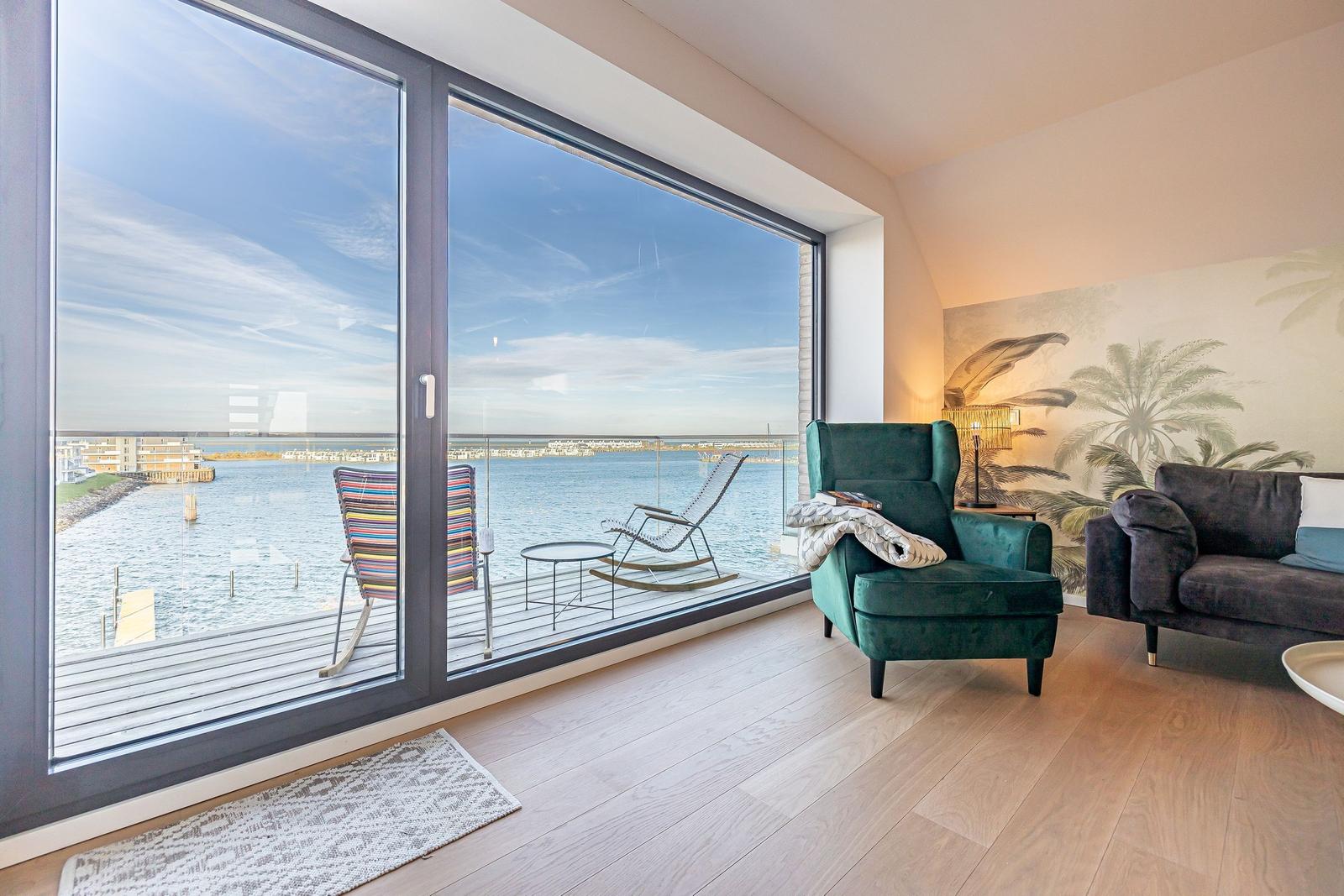 Wohnzimmer mit Meerblick, grüner Sessel und Balkon mit Liegestühlen.