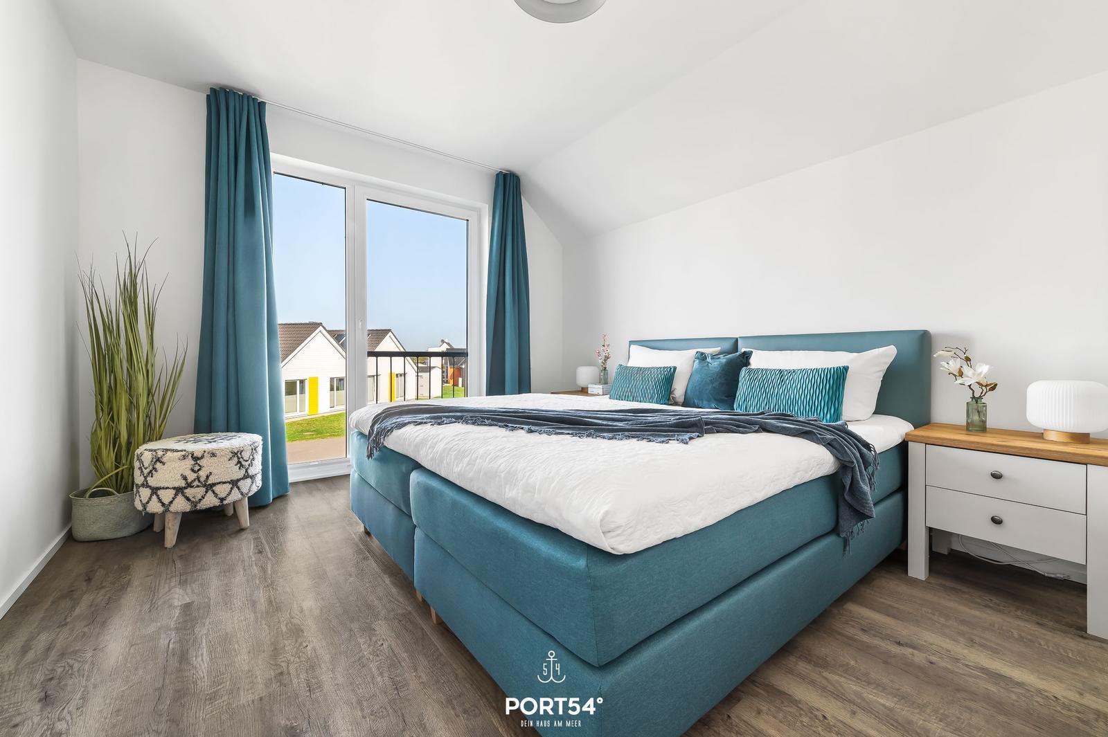 Schlafzimmer mit blauem Bett, Fensterblick und Holzboden.
