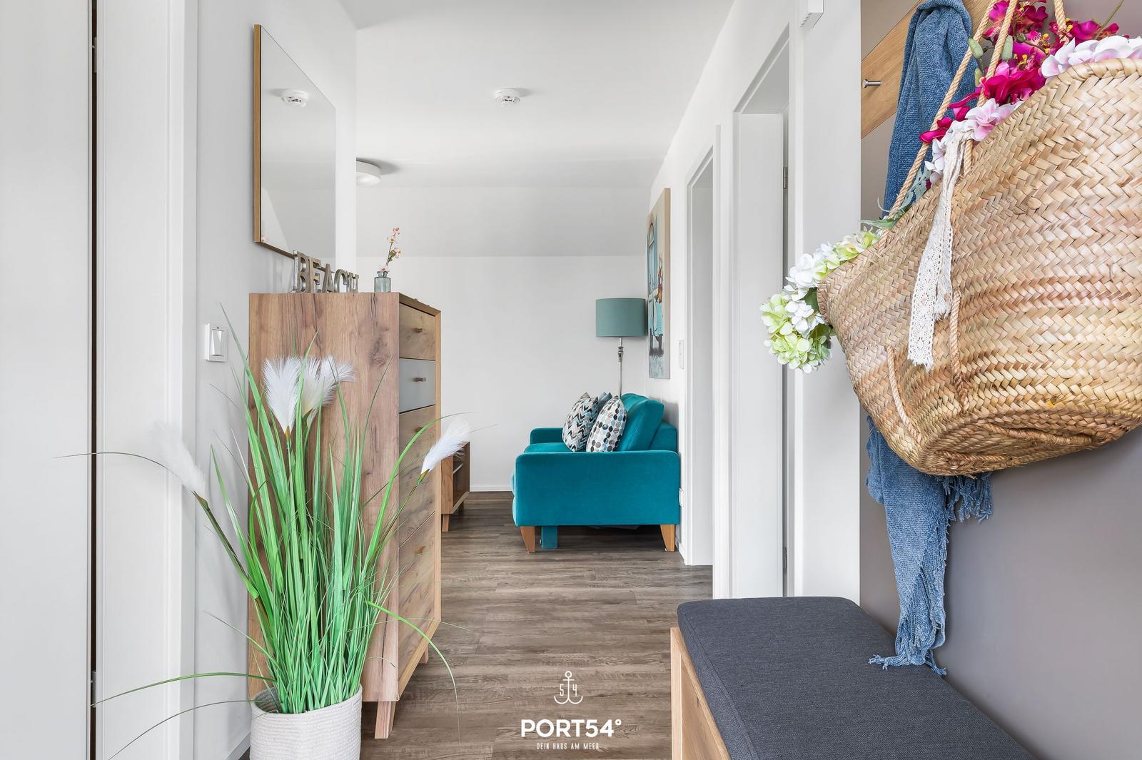Eingangsbereich mit Holzschrank, Pflanze und blauem Sofa im Hintergrund.