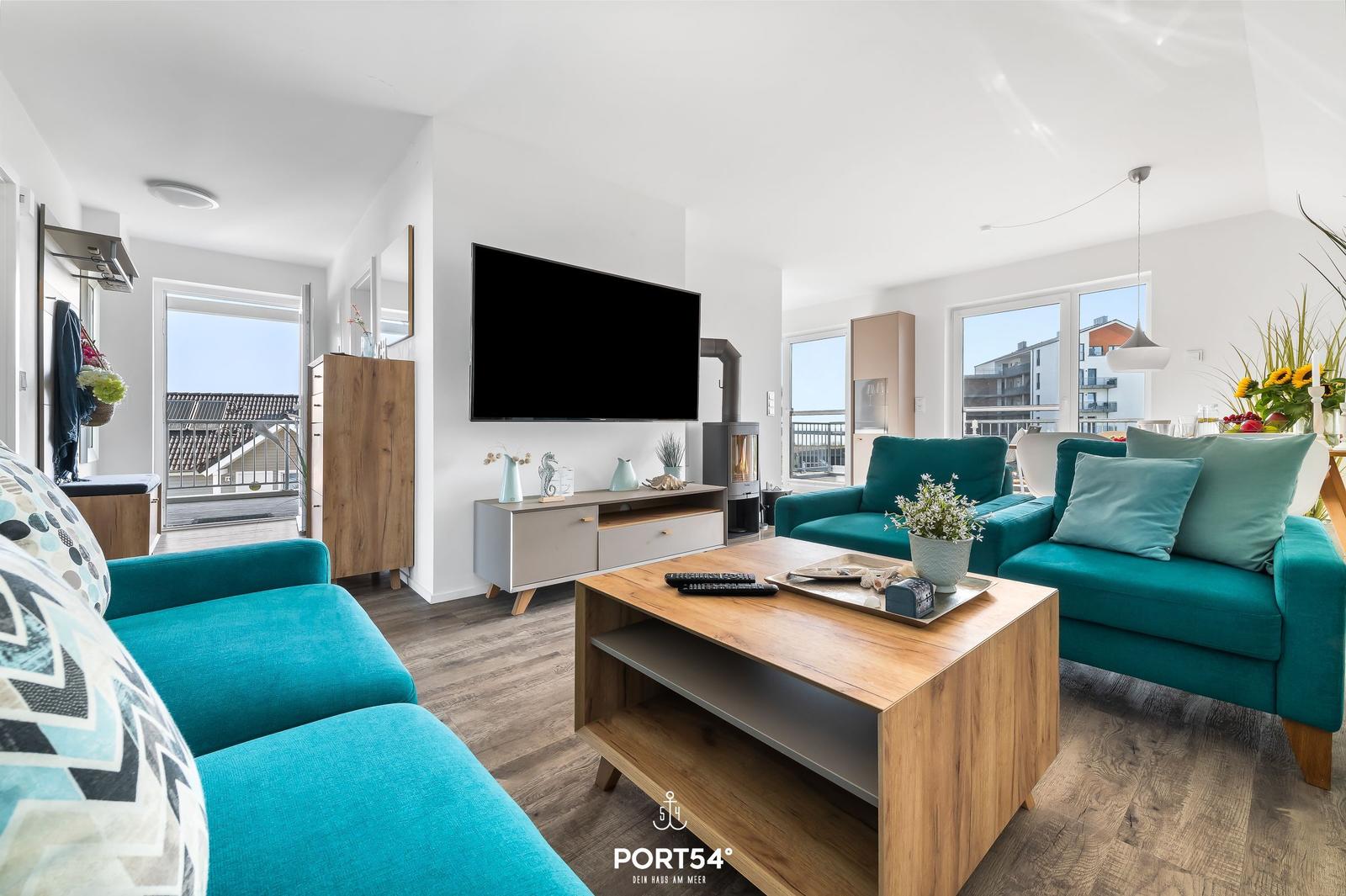 Wohnzimmer mit türkisfarbenen Sofas, Holzfußboden und Fernseher an der Wand.