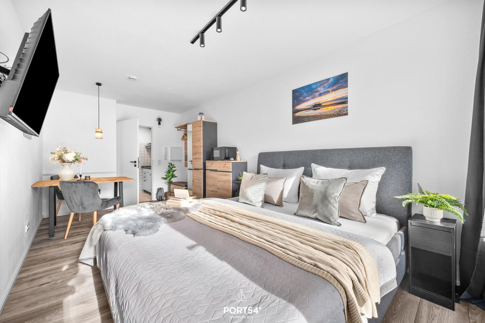 Schlafzimmer mit Bett, Nachttisch, Fernseher und Essbereich.