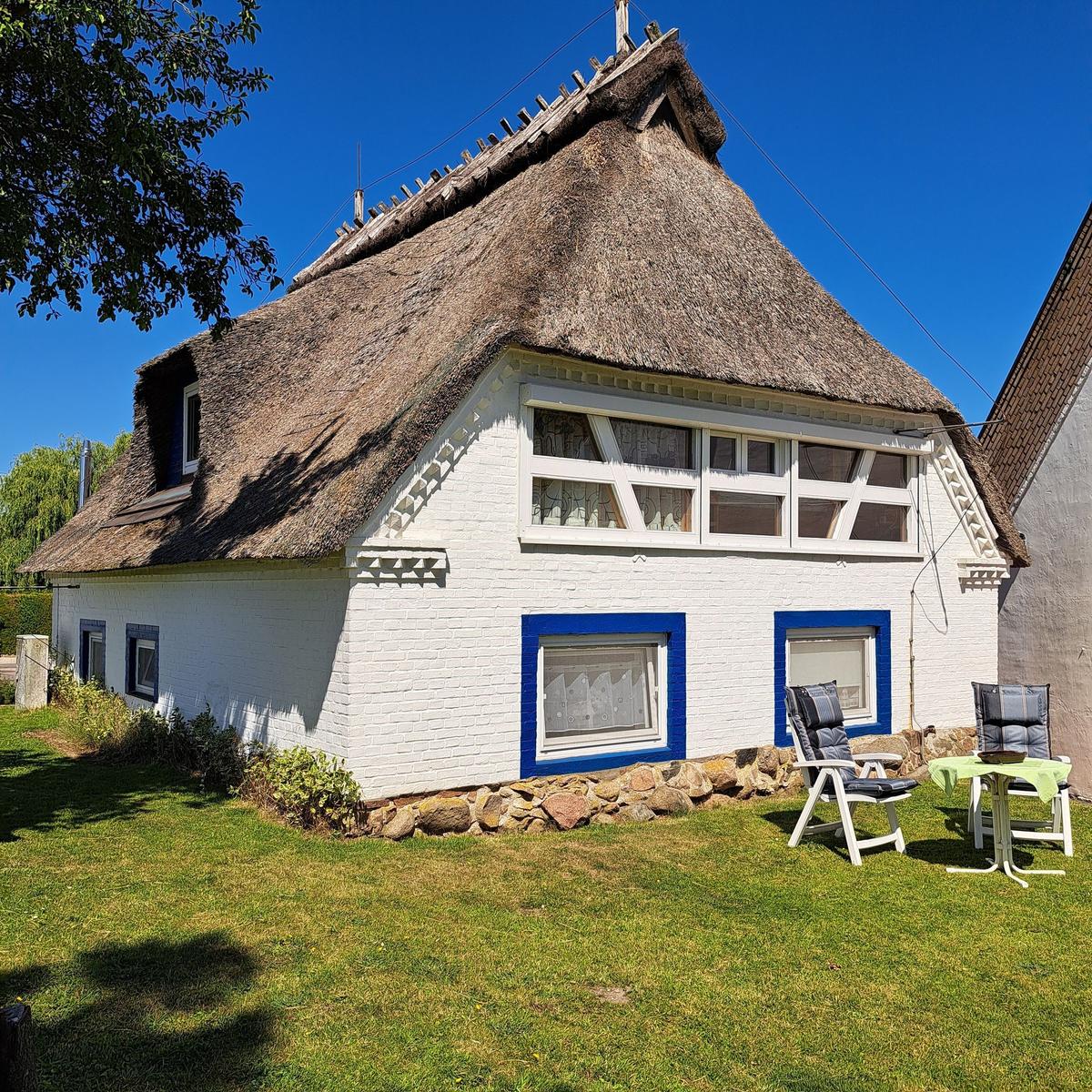 A white house with thatched roof, blue window frames, and garden furniture in the front yard.