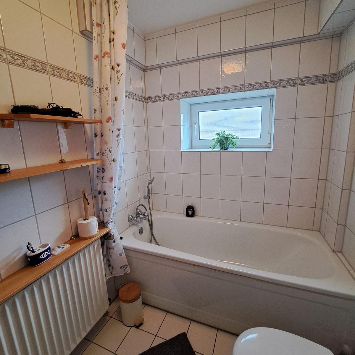 Bath with bathtub, window, and wooden shelves on the wall.