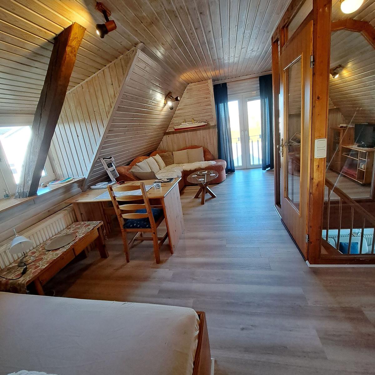 Living room with sleeping area, wooden ceiling, and balcony door.