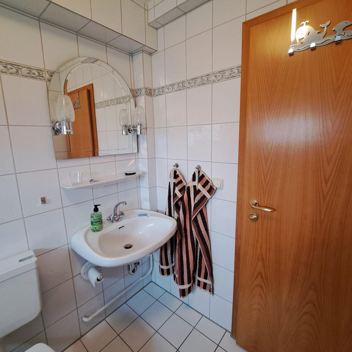 Bathroom with sink, mirror, and toilet. Wooden door with wall lamp.