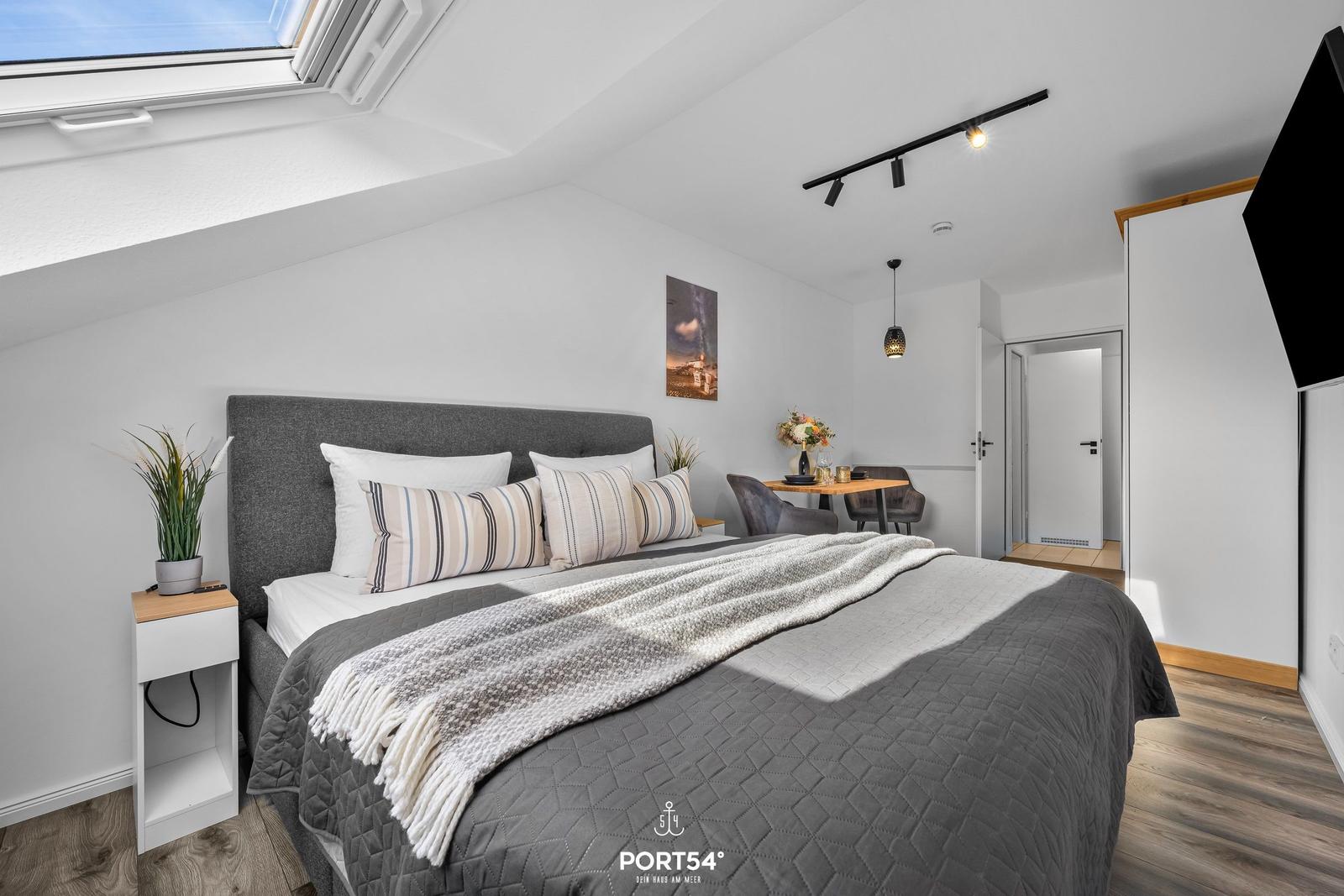Schlafzimmer mit Dachfenster, Bett, Tisch und Stühlen.