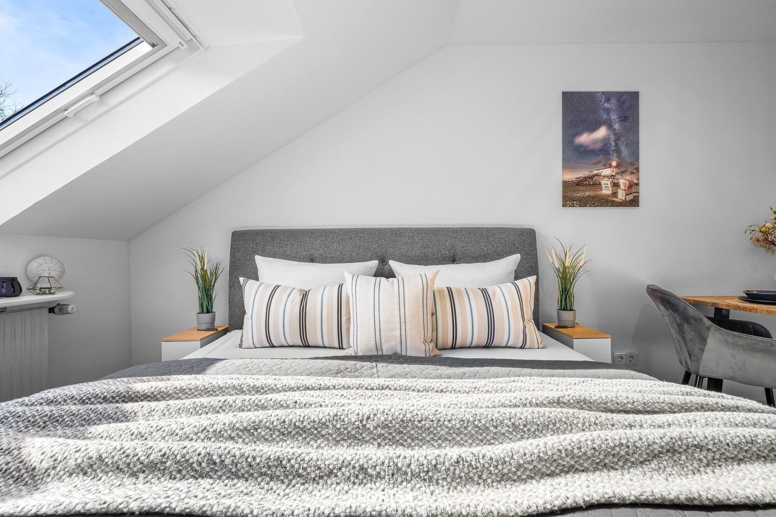 Schlafzimmer mit Dachschrägen, Bett, Nachttischen und Fenster.