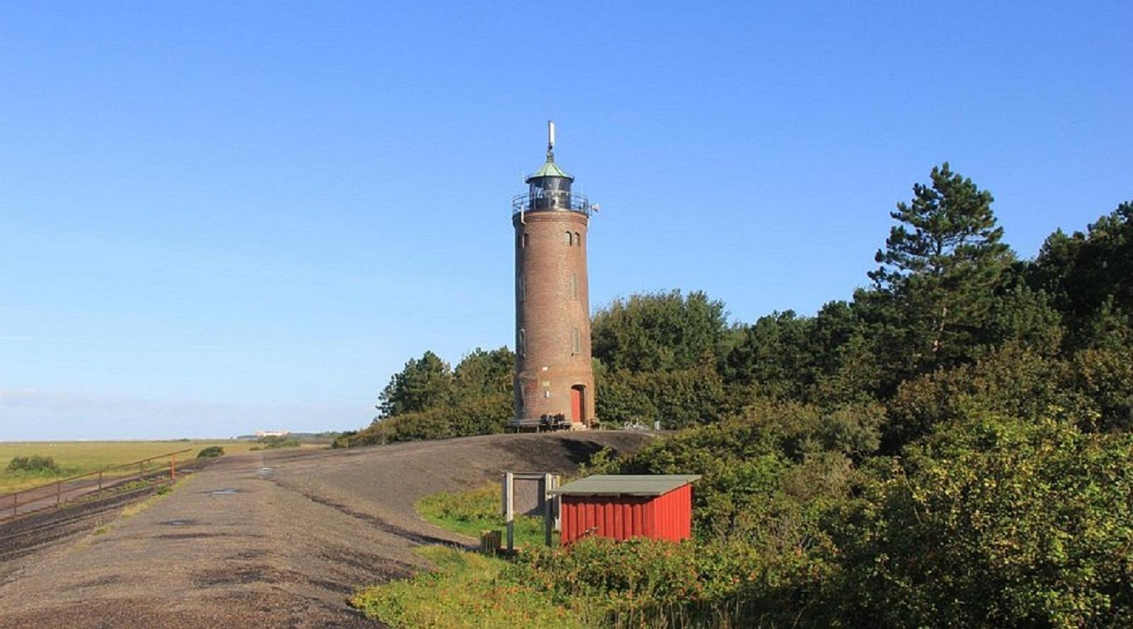 Roter Leuchtturm auf grüner Anhöhe mit Wald und Weg
