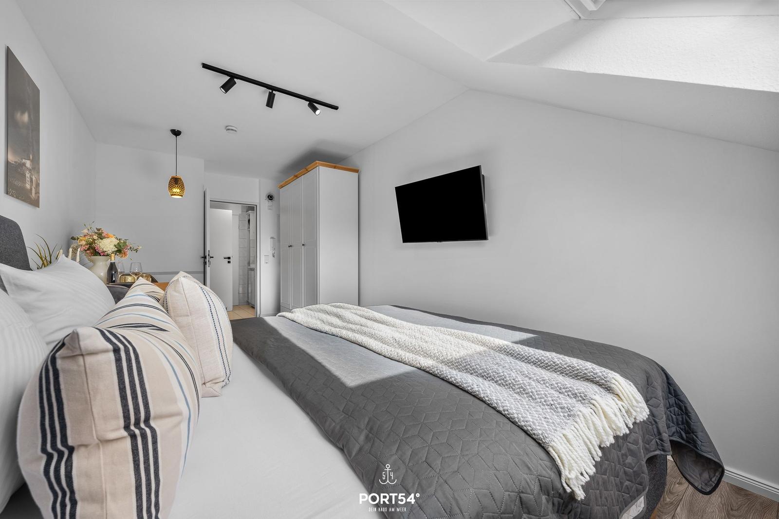 Schlafzimmer mit Bett, Fernseher und Kleiderschrank.