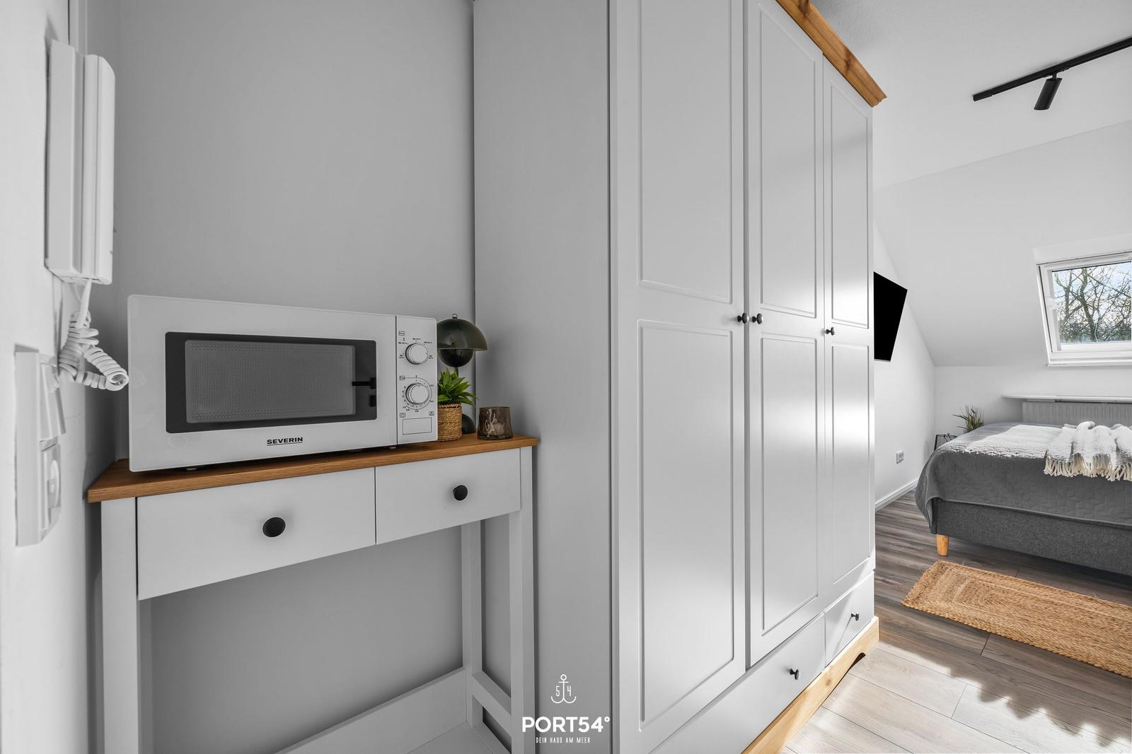 Schlafzimmer mit Dachschräge, Bett, Kleiderschrank und Mikrowelle auf Holzkonsole.