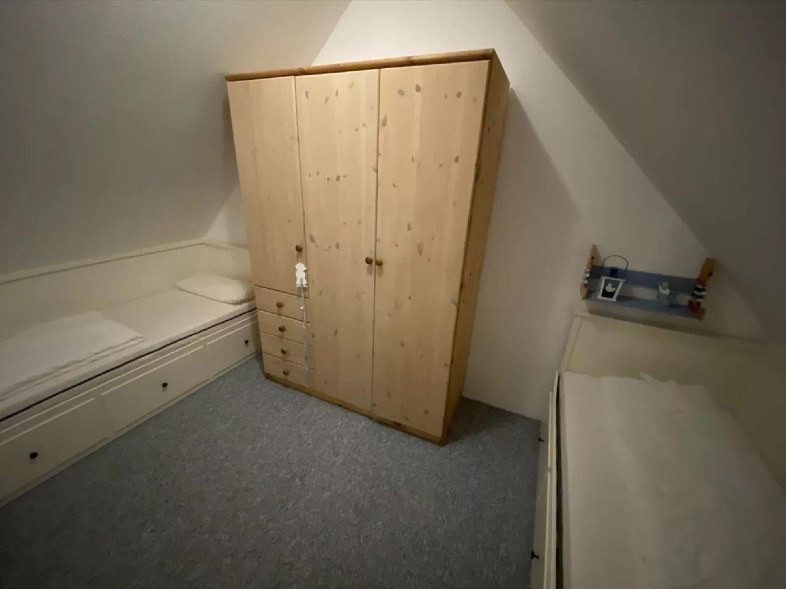 Zimmer mit Schlafcouch, Kleiderschrank und Kinderbett unter Dachschrägen.