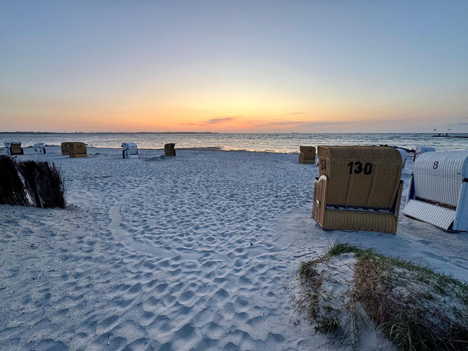 Strand mit Liegestühlen und Sonnenuntergang am Horizont.