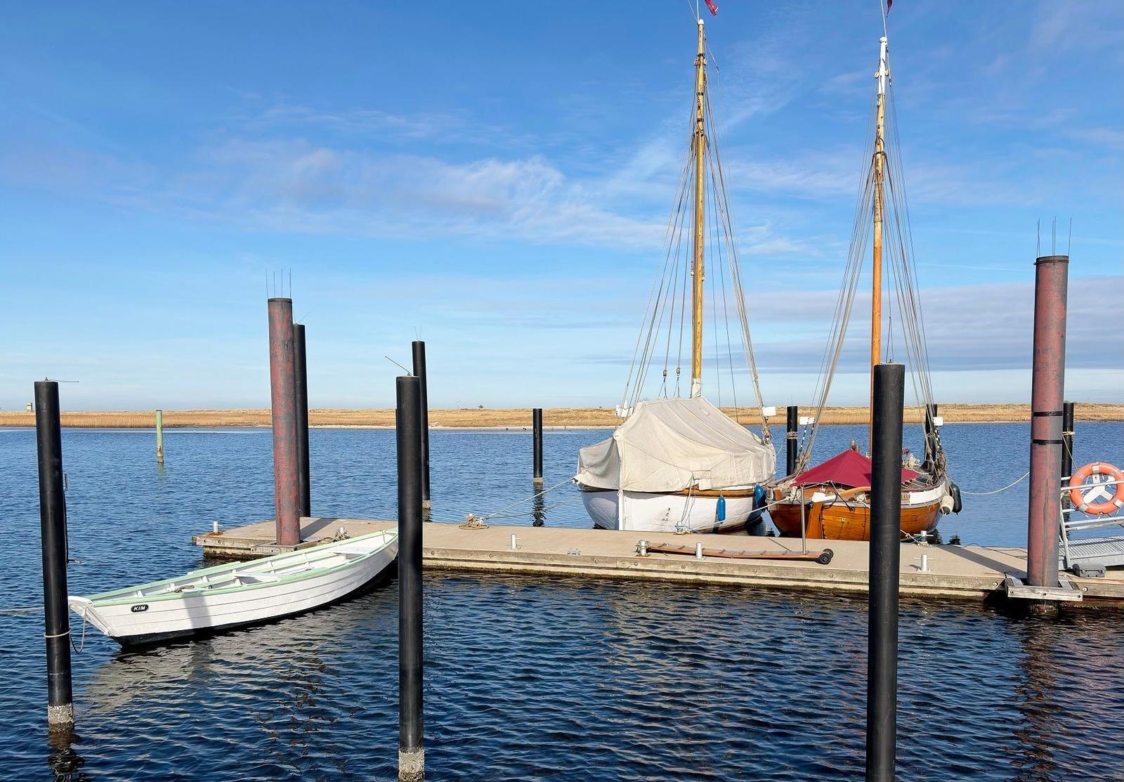 Hafen mit zwei Segelbooten und einem kleinen Boot im Wasser.
