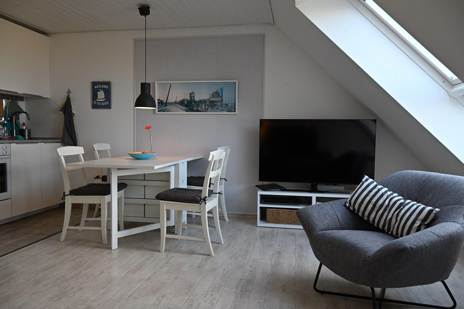 Wohnbereich mit Esstisch, TV und Sessel unter Dachschräge.