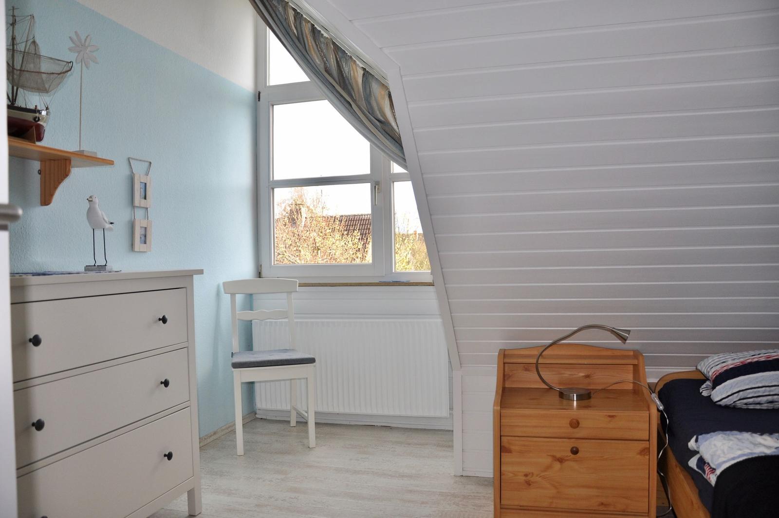 Schlafzimmer mit Bett, Nachttisch, Stuhl und Schrank. Fenster mit Blick nach draußen.