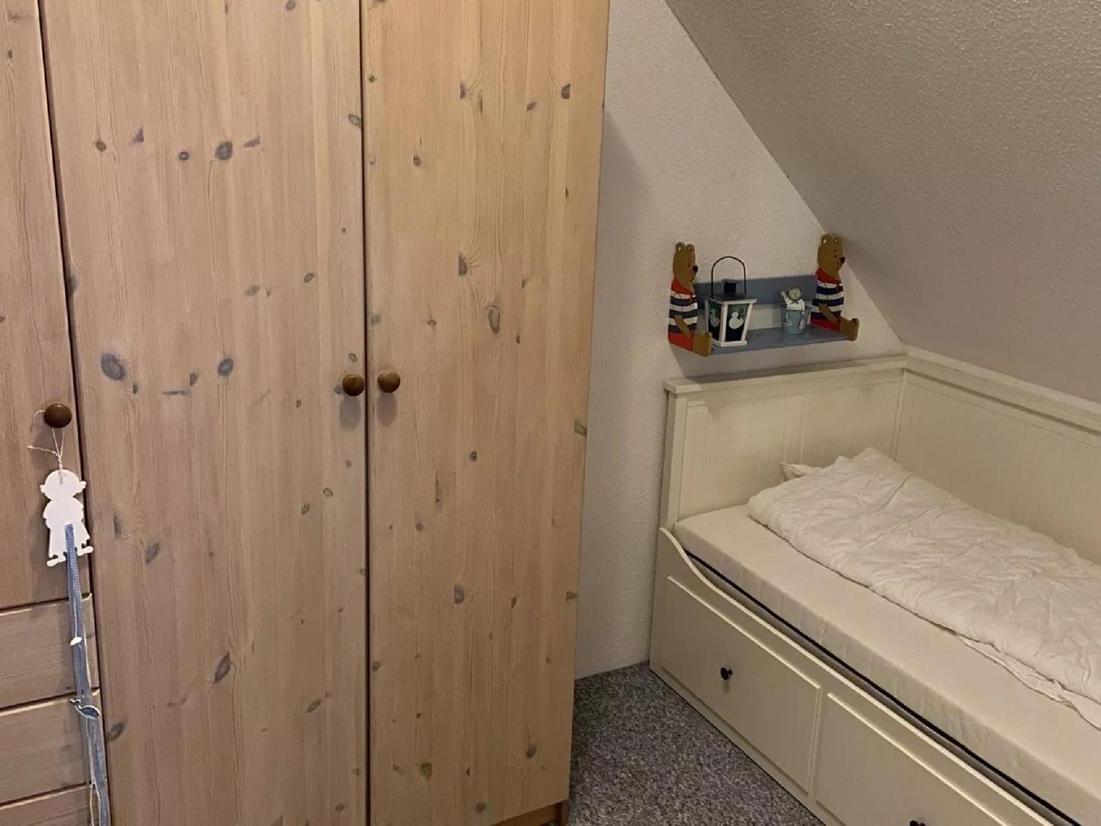 Kleines Schlafzimmer mit Dachschrägen, weißem Bett und Holzschrank.