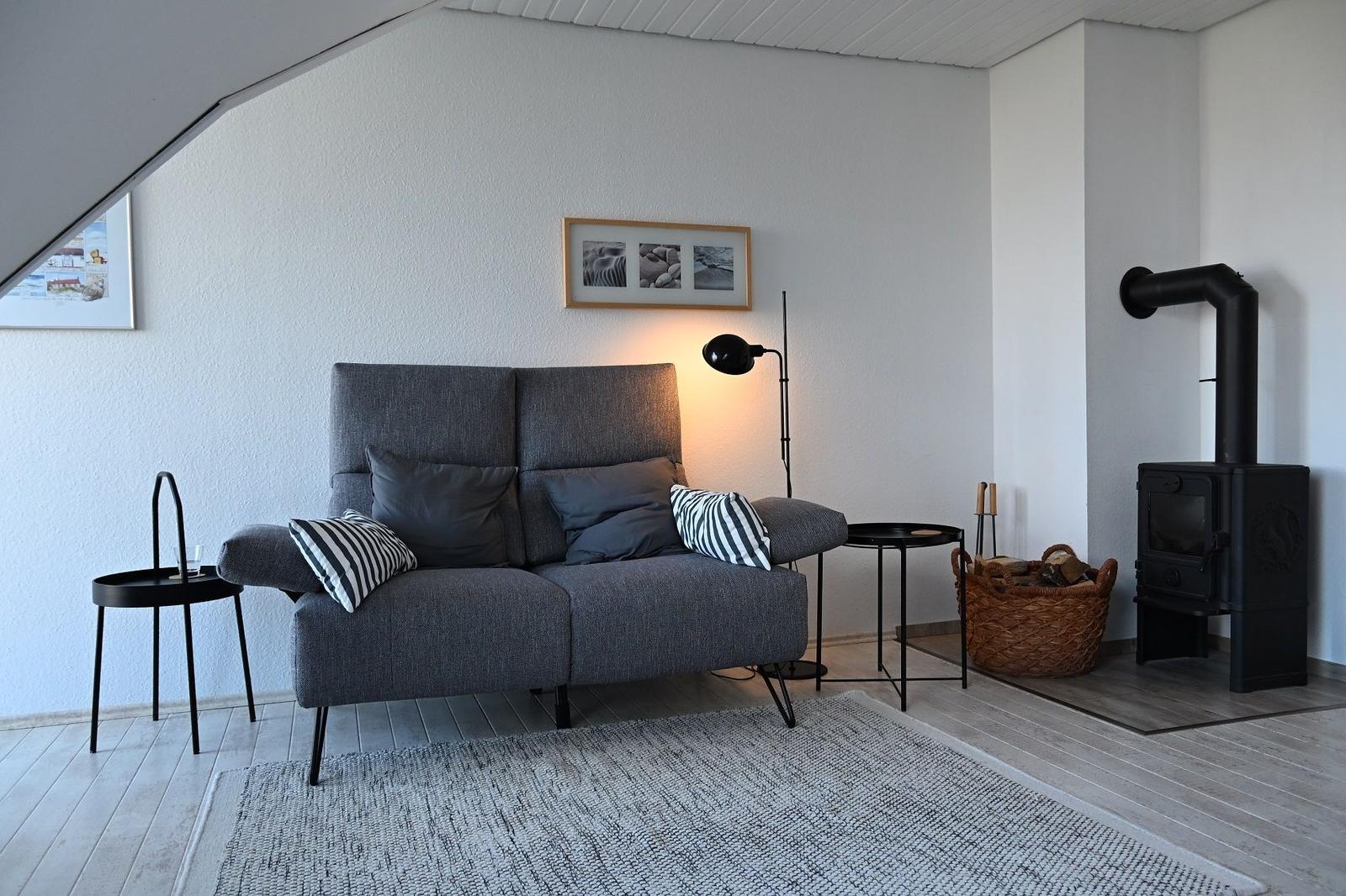 Ein Wohnzimmer mit grauem Sofa, Stehlampe und Kaminofen.