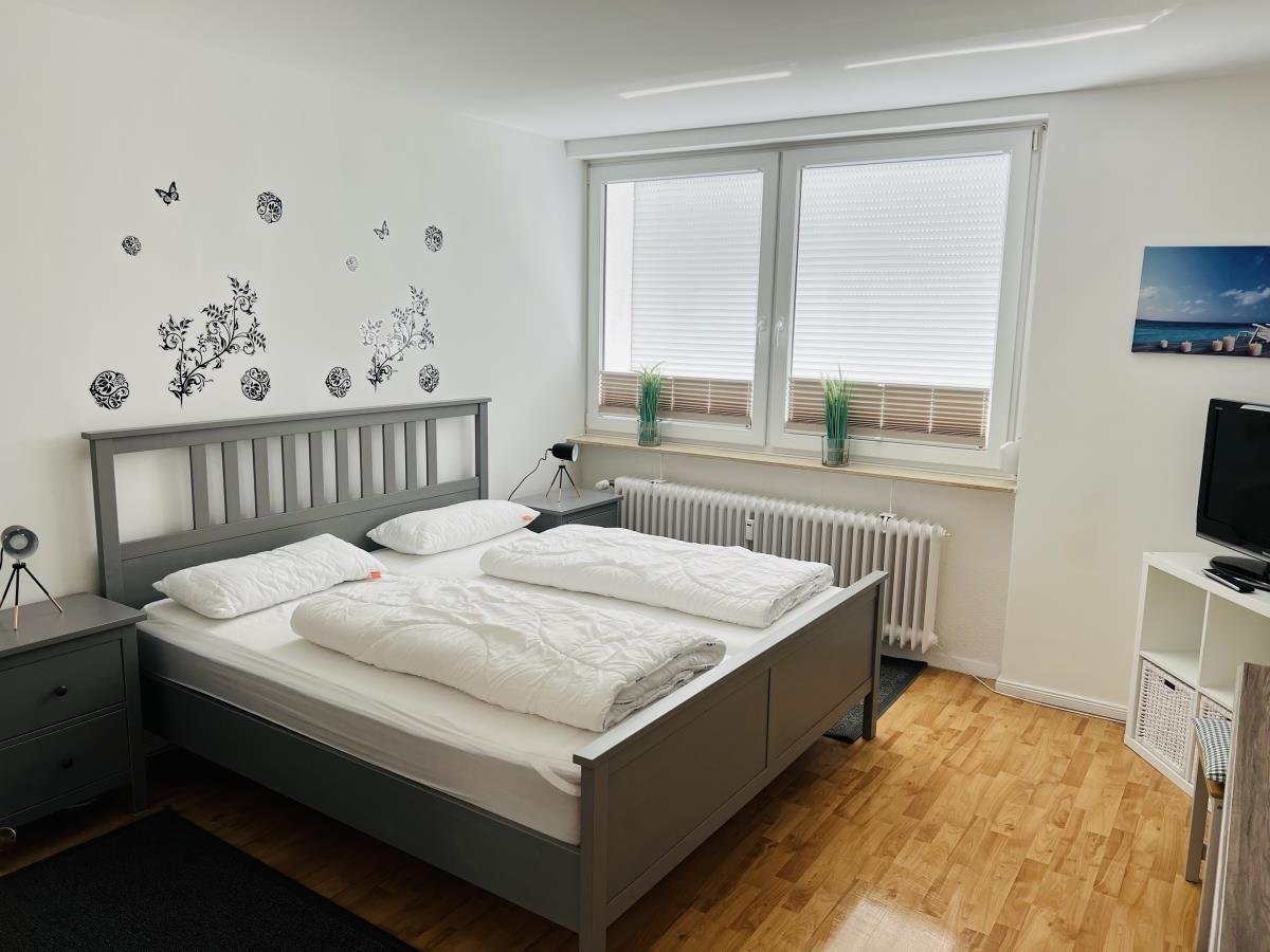 Bedroom with double bed, window, TV and wooden floor.