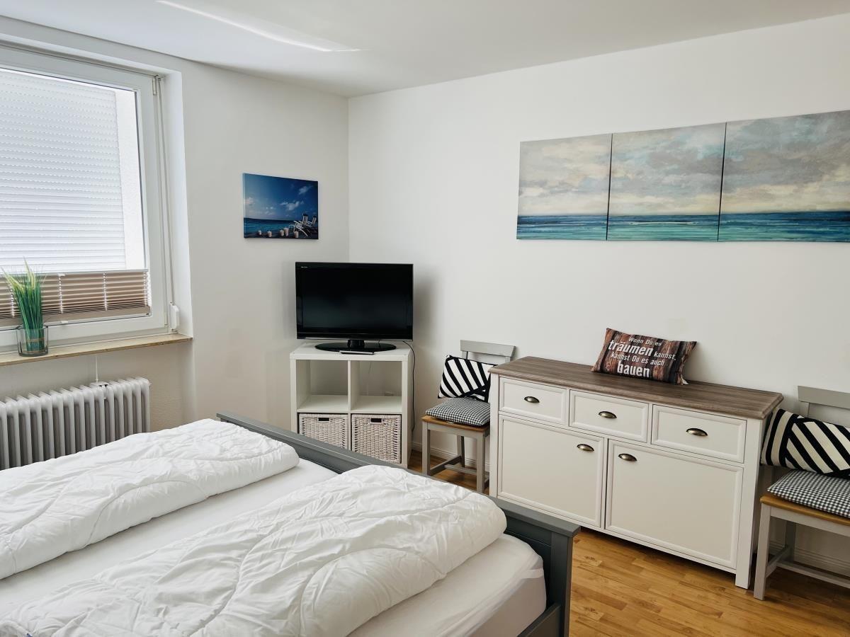 Bedroom with bed, TV, and cabinets. Wall art shows sea.