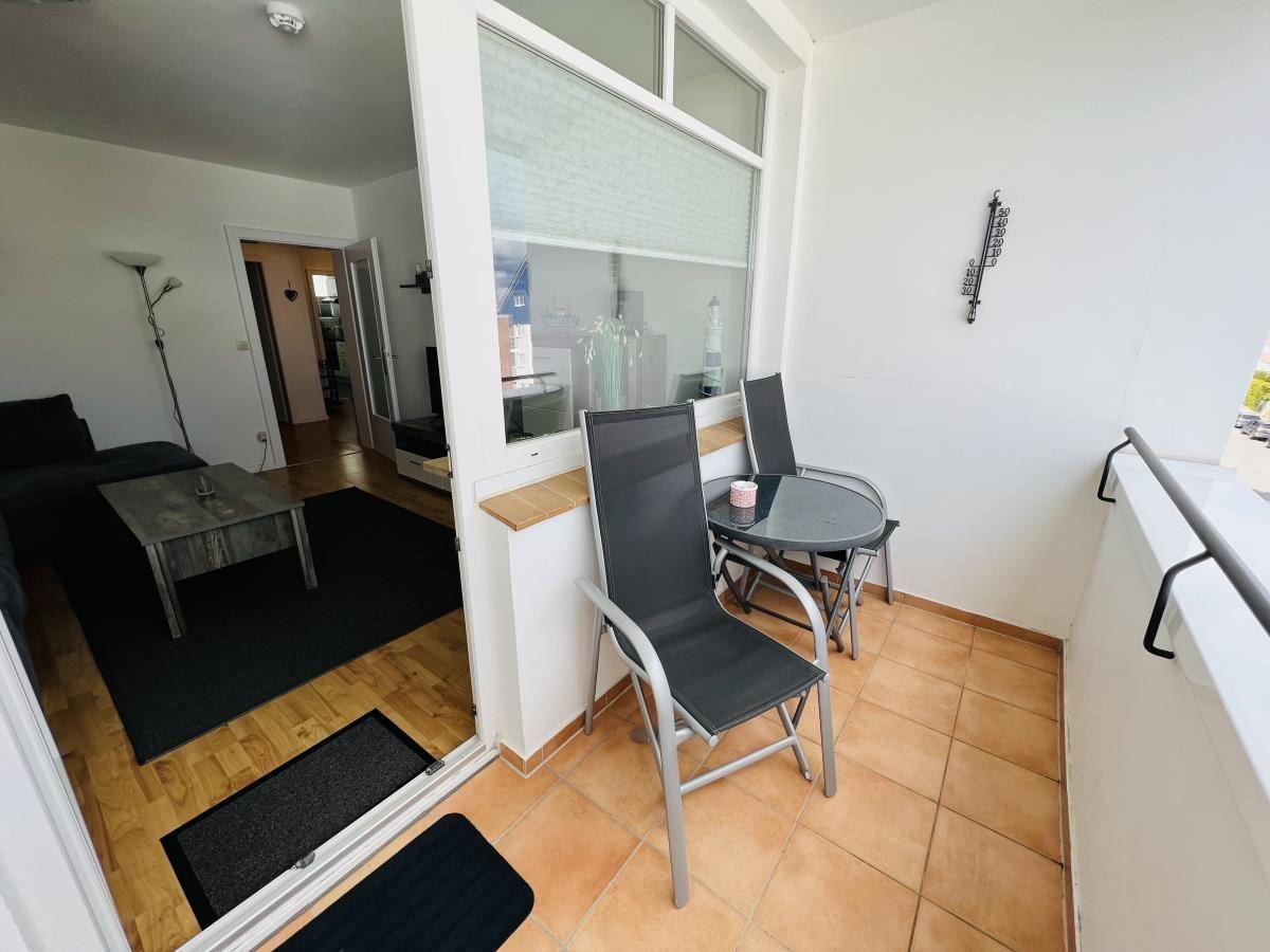 Balcony with table and chairs, view into living room with sofa and coffee table.
