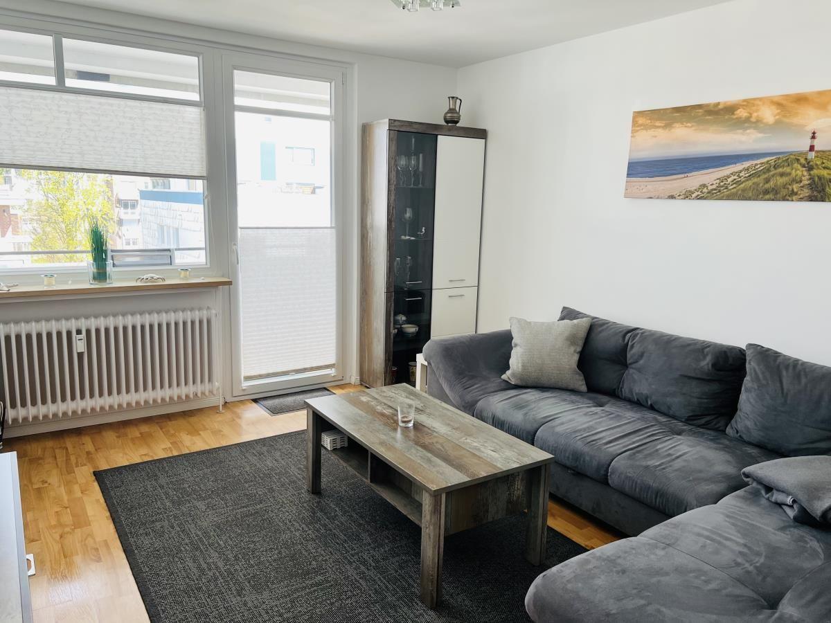 Living room with sofa, table, and windows. Wall picture and cabinet are visible.
