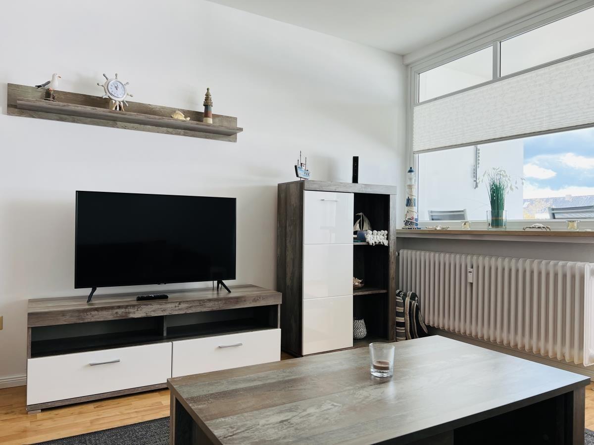 Living room with TV, table, and window. Furniture is modern and simple.
