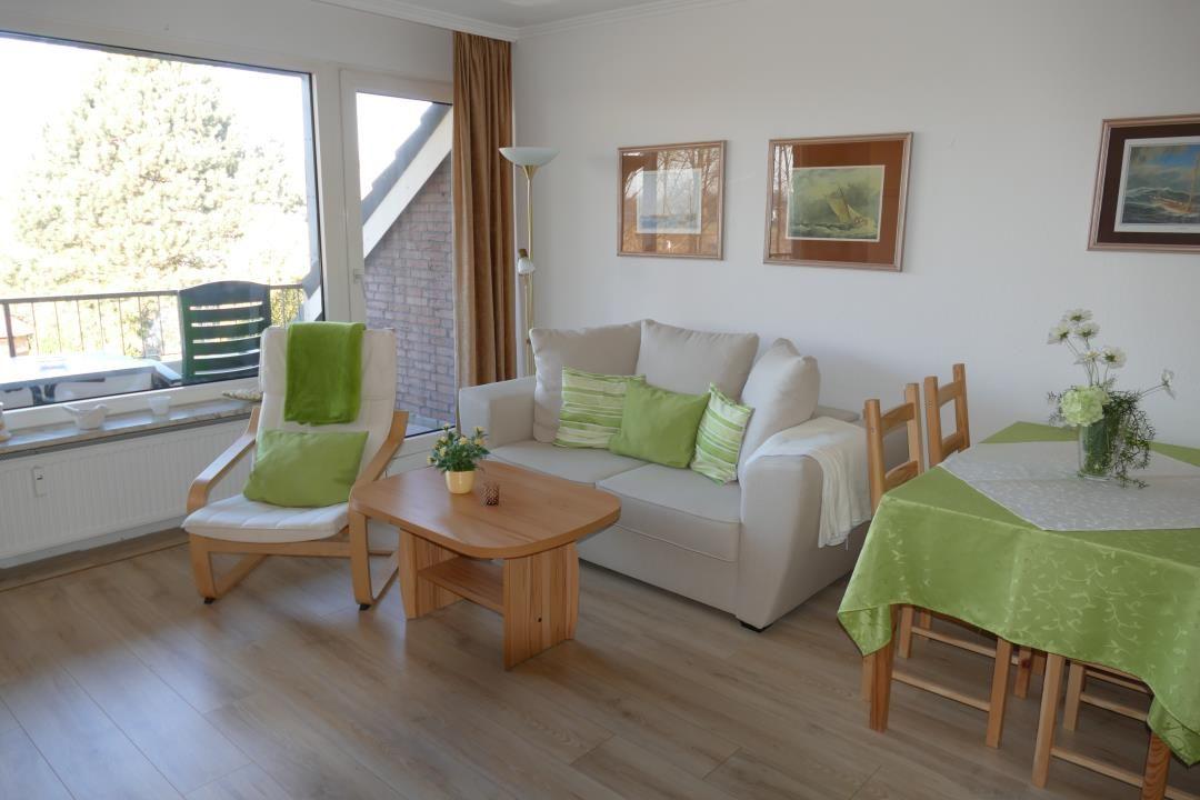 Wohn- und Essbereich mit Sofa, Stuhl und Tisch. Grüne Tischdecke und Kissen. Fenster mit Blick auf Balkon.