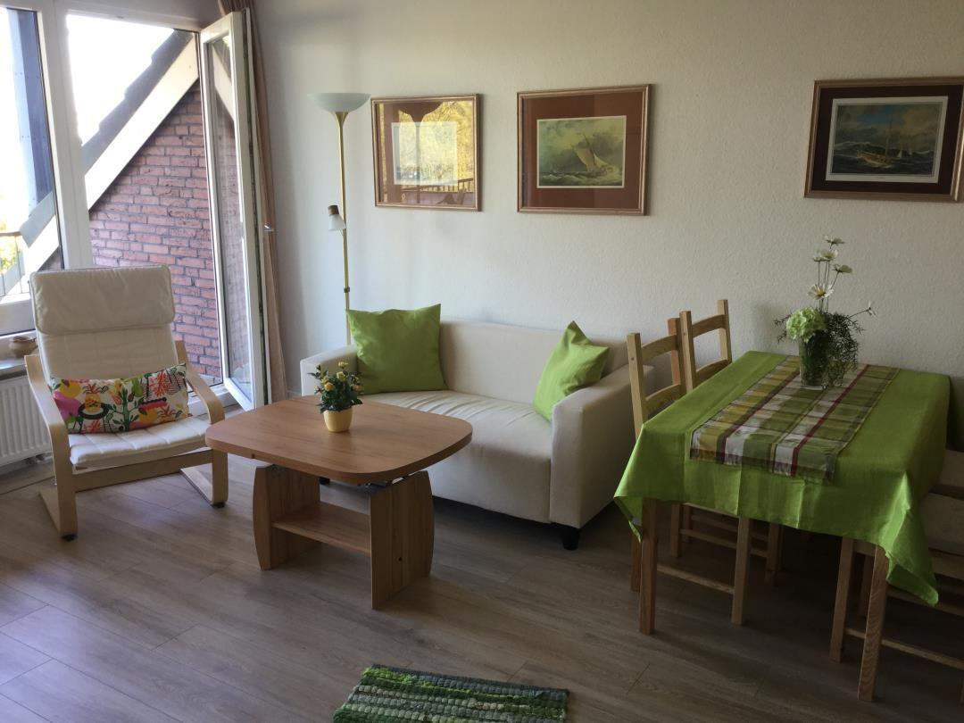 Wohn- und Essbereich mit Sofa, Stuhl, Tisch und Wandbildern.