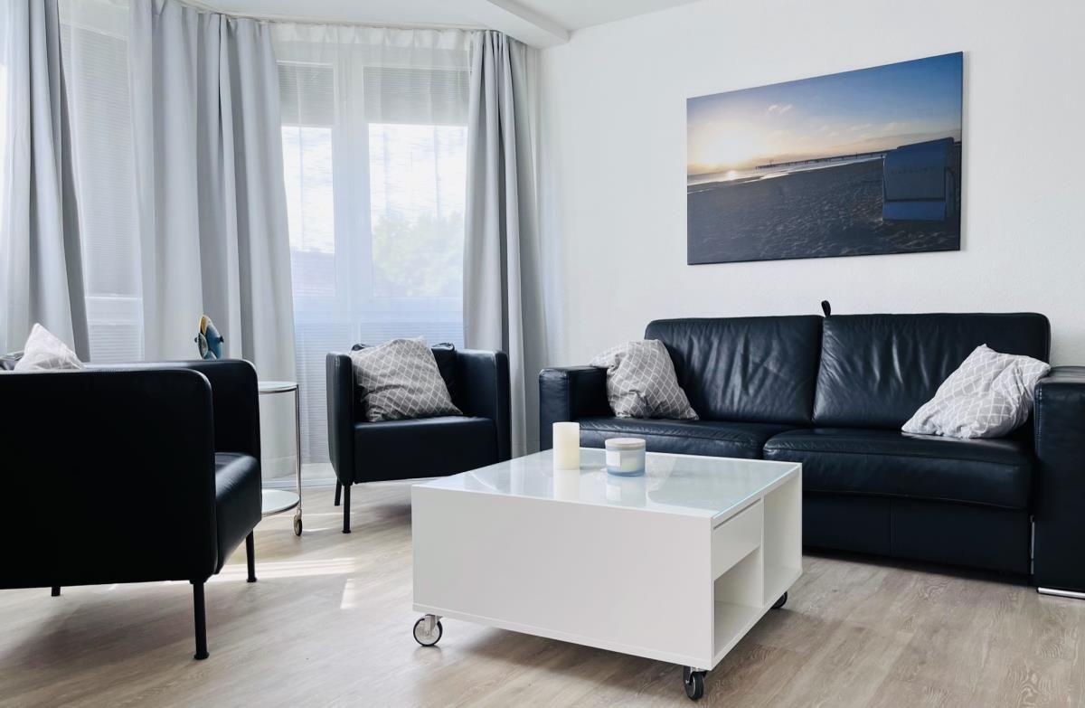 Living room with black sofa, two chairs, and white coffee table. Wall art shows beach.