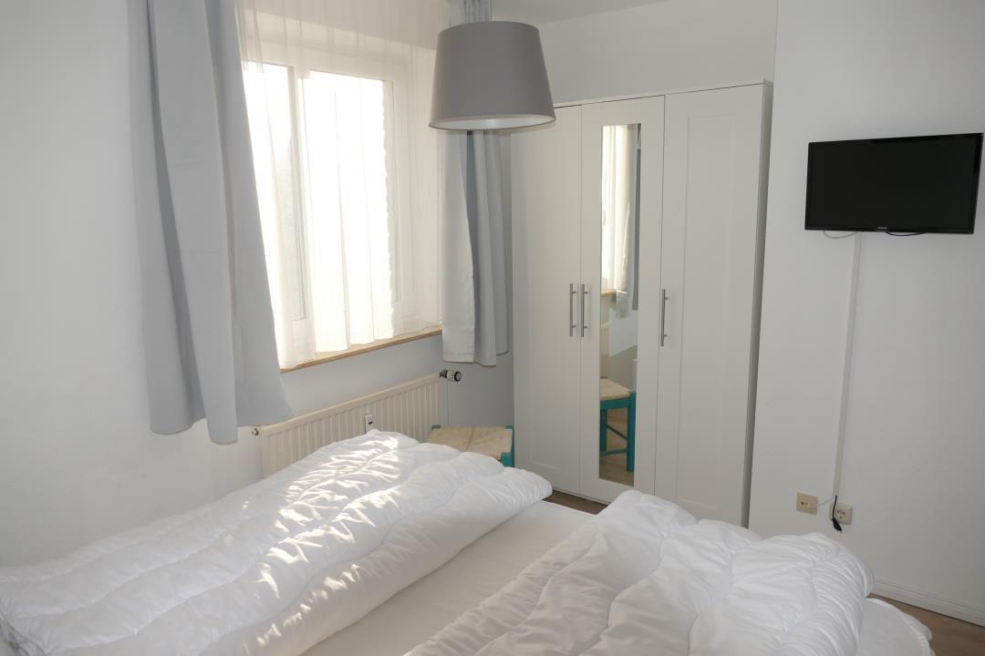 Bedroom with bed, window, wardrobe, and wall-mounted TV.