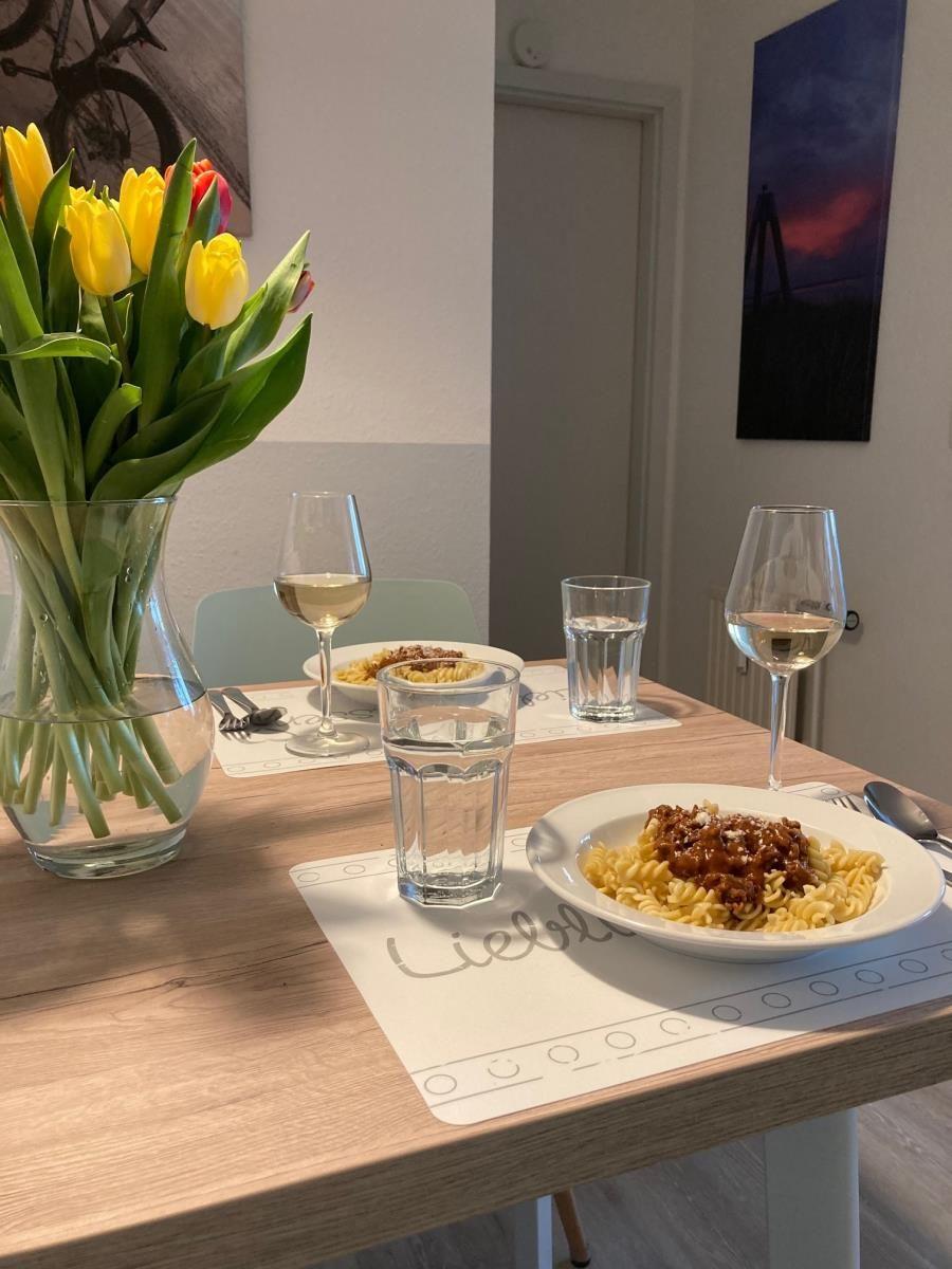 Table with pasta, wine, and tulips in dining area.