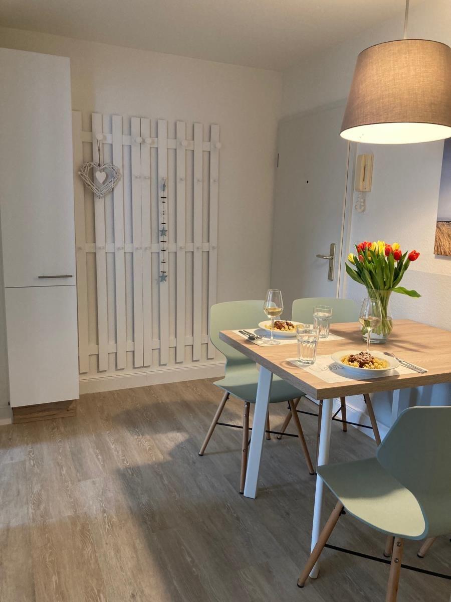 Dining table with chairs, flowers, and pendant light in a room with wooden floor and white walls.
