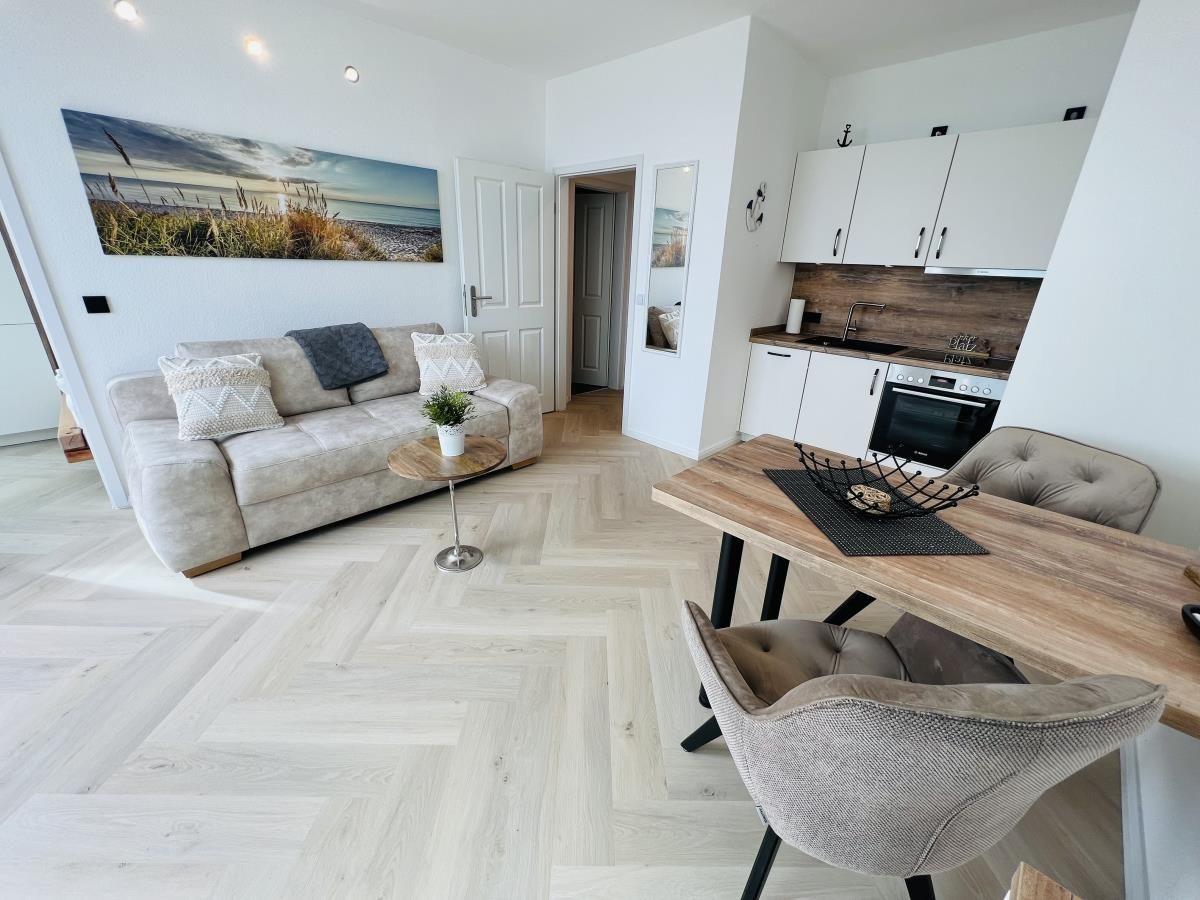 Wohnzimmer mit Sofa, Esstisch und Küchenbereich. Holzfußboden und Wandbild.