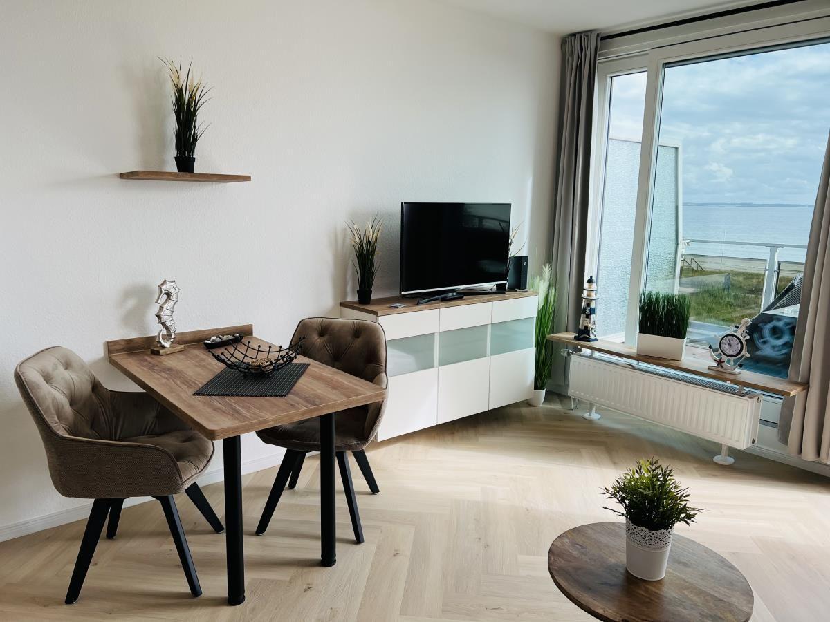 Wohn- und Essbereich mit TV, Tisch und Stühlen. Blick aufs Meer durch große Fenster.