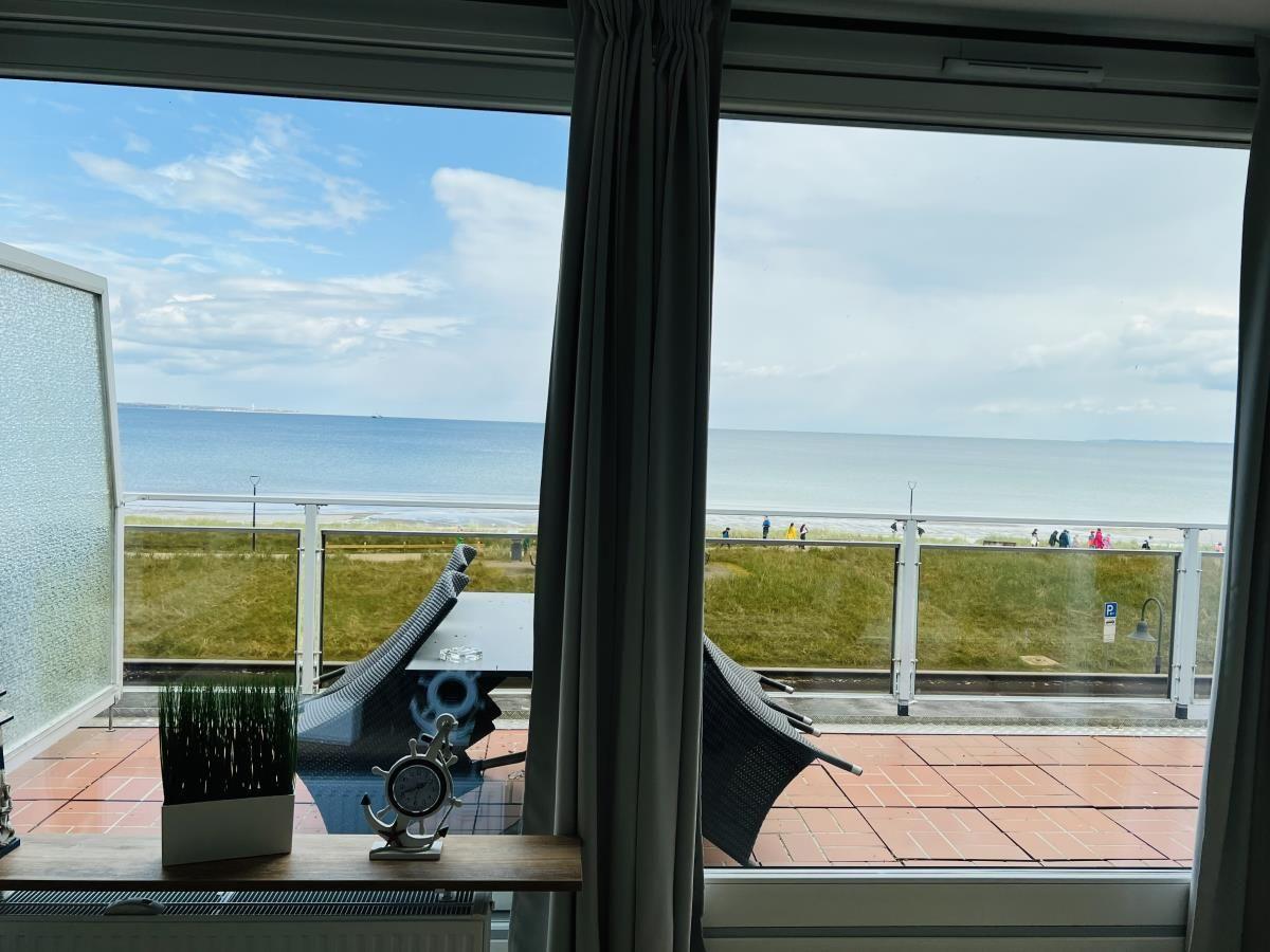 Blick auf das Meer von einer Terrasse mit Liegestühlen und Glasgeländer.