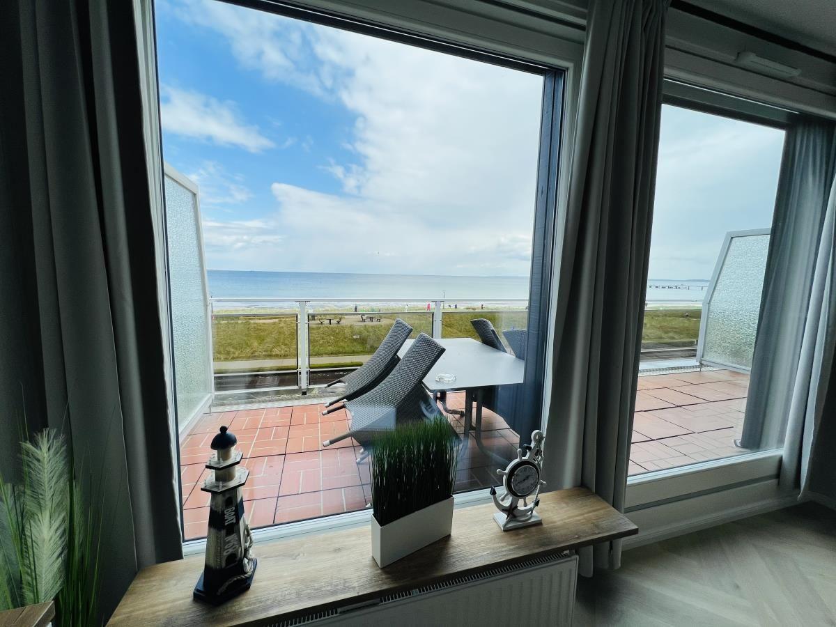 Terrasse mit Tisch und Stühlen bietet Meerblick. Fenster mit Vorhängen und Dekoration.