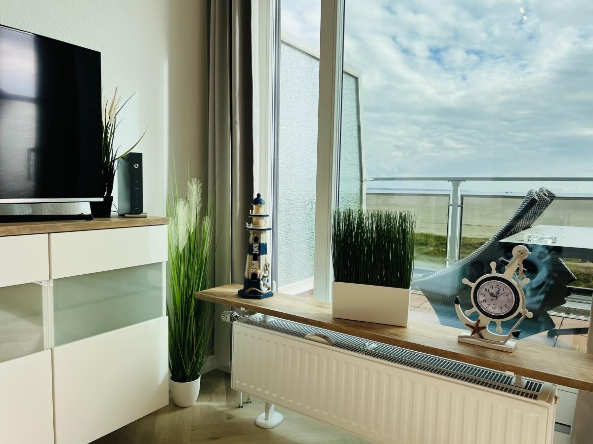 Wohnzimmer mit TV, Pflanzen und Meerblick durch große Fenster.