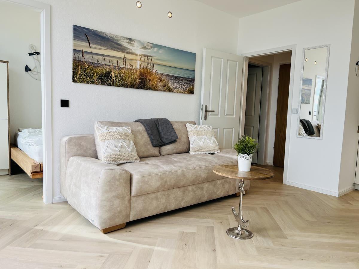 Wohnzimmer mit Sofa, Wandbild und Holzboden. Blick in Schlafzimmer und Bad.