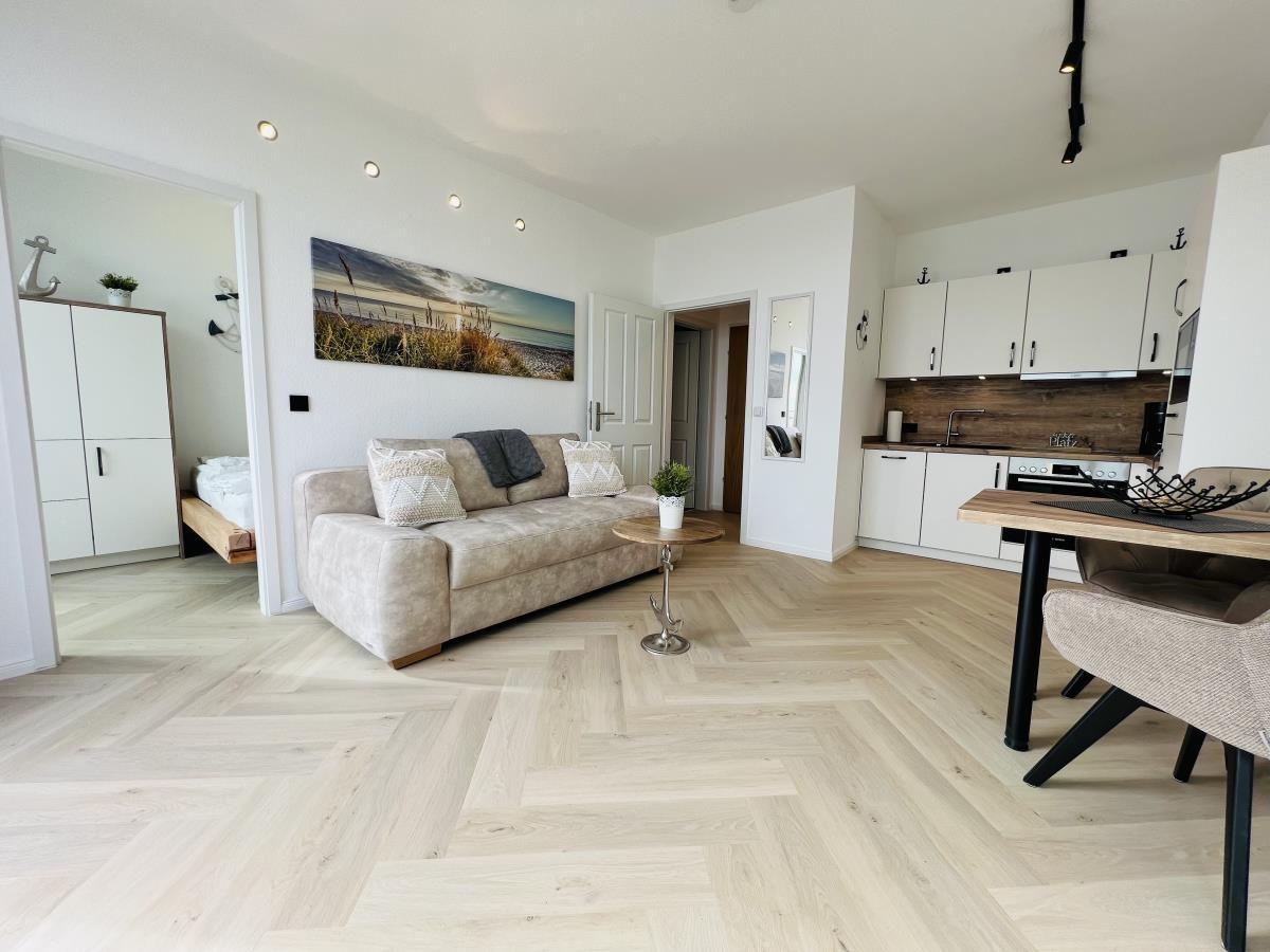 Wohnung mit Wohn- und Essbereich, Küche und Schlafzimmer. Holzfußboden und helle Wände.