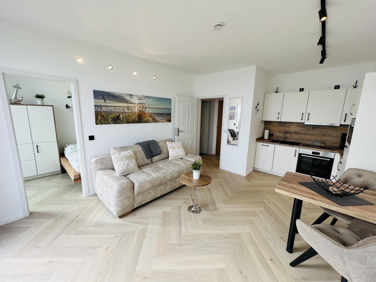 Wohnung mit Wohnzimmer, Küche und Schlafzimmer. Holzfußboden und weiße Wände.