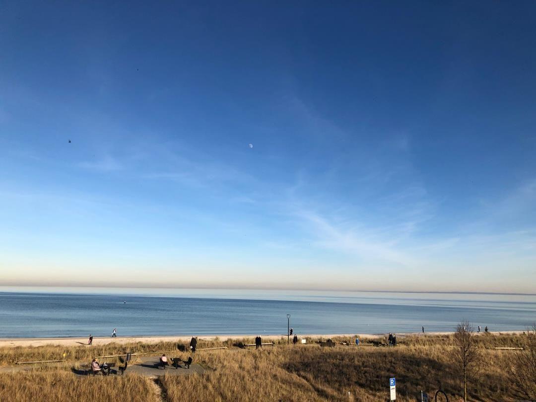 Strand mit Dünen und klarem Himmel. Menschen genießen die Aussicht.
