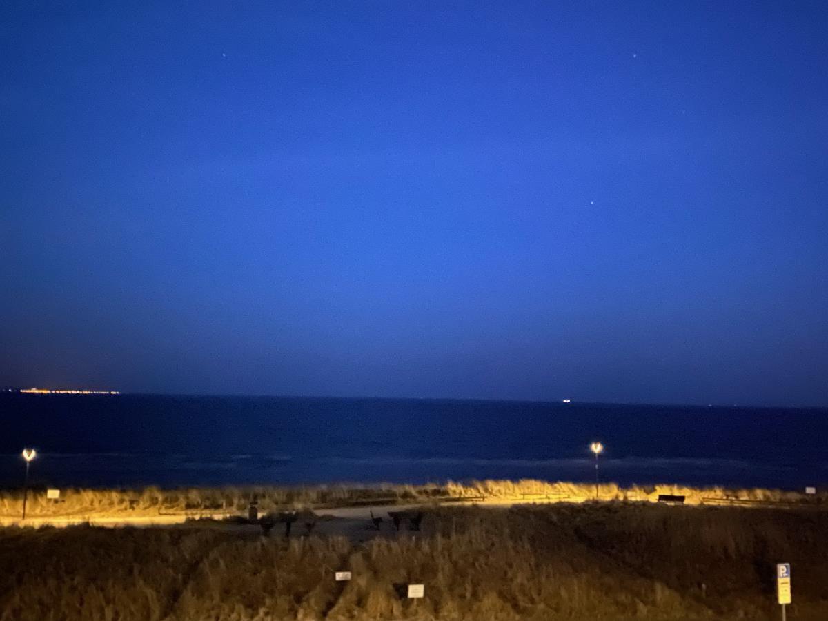 Nachtansicht vom Strand mit beleuchteten Dünen und Meer im Hintergrund.